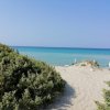 Spiaggia con sabbia chiara, mare turchese e ombrelloni bianchi. Vegetazione verde sulla sinistra.