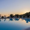 Piscina tranquilla al tramonto, con ombrelloni e palme visibili sullo sfondo.