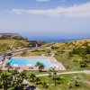 Piscina all'aperto con lettini, circondata da colline verdi e vista sul mare.