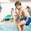 Ragazzo in aria mentre salta in piscina affollata.