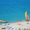 Spiaggia con sabbia bianca, barche, pedalò e una barca a vela colorata sul mare turchese.