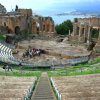 Antico teatro in pietra con gradinate semicircolari, vista mare.
