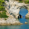 Arco naturale di roccia sopra il mare con vegetazione verde.