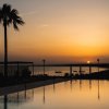 Tramonto sul mare con piscina in primo piano e una palma.