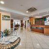 Reception di un hotel con bancone in legno, tavolo con giornali e decorazioni floreali.