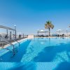 Piscina all'aperto con vista sul mare, palme e sedie a sdraio.
