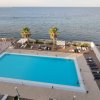 Vista dall'alto di una piscina rettangolare vicino alla costa, con sedie a sdraio e palme.