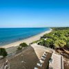 Vista aerea di una spiaggia sabbiosa con mare calmo e una pineta.