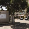Ingresso di un hotel con segnaletica, auto parcheggiate e bandiere.