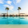 Piscina all'aperto con due palme e cielo azzurro riflesso nell'acqua.