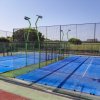 Campi da padel con recinzioni in vetro e pali di illuminazione verde.