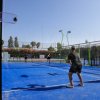 Quattro giocatori su un campo da padel blu, illuminato dal sole.