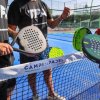 Tre persone con racchette da padel sopra la rete, su campo blu.