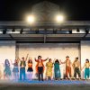 Persone in abiti colorati si tengono per mano su un palco, salutando.