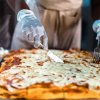 Mani con guanti affettano una pizza rettangolare su un vassoio.