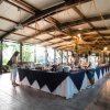 Persone servono cibo da un lungo buffet coperto da tovaglie blu e bianche sotto un tetto aperto.