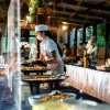 Buffet in un ristorante con una chef che serve un cliente, entrambi indossano mascherine.