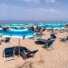 Spiaggia sabbiosa con ombrelloni e lettini blu, mare sullo sfondo.