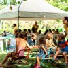 Bambini giocano in un parco sotto un gazebo, con adulti seduti ai tavoli.