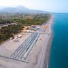 Vista aerea di una lunga spiaggia con ombrelloni blu e mare calmo.
