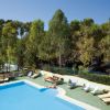 Piscina all'aperto circondata da lettini su cui prendono il sole diverse persone. Alberi intorno.