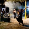 Musicisti suonano all'aperto, una persona danza al centro della scena illuminata.