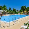 Piscina all'aperto con sdraio e piante, persone che nuotano.
