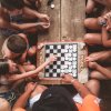 Bambini intorno a una scacchiera su un tavolo di legno, concentrati nel gioco.
