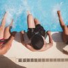 Tre persone sedute sul bordo di una piscina, con i piedi nell'acqua.