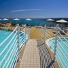 Piscina con passerella e ombrelloni vista mare.