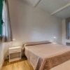 Un letto matrimoniale con copriletto beige, due comodini bianchi e due finestre con tende.