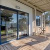 Terrazza con tavolo e sedie su pavimento in legno, vista giardino e porta finestra riflettente.