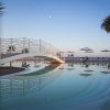 Piscina con ponte curvo e ombrelloni, alberi al tramonto.