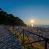 Sentiero costiero al tramonto, con spiaggia e ombrelloni.