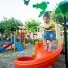 Bambina su scivolo arancione in parco giochi.