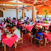 Persone sedute a tavoli con tovaglie rosse in un ristorante coperto con travi di legno.