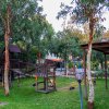 Area giochi all'aperto con strutture in legno tra alberi e prato.