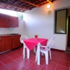 Cucina esterna con tavolo rosso, sedie bianche e credenze in legno.
