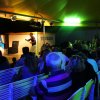 Una performance su un palco sotto una tenda con spettatori seduti.