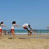Persone che fanno acrobazie sulla spiaggia davanti al mare.