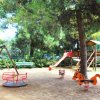 Un parco giochi con altalena, giostra rossa e scivolo tra alberi.