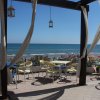 Tavoli esterni con vista mare, tende e lanterne, spiaggia con ombrelloni sullo sfondo.