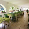 Sala da pranzo interna con tavoli apparecchiati, sedie verdi, piante in vaso e archi.