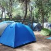 Tende blu e verdi montate tra alberi in un'area di campeggio.