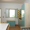 Una cucina con mobili azzurri, tavolo bianco e finestra aperta.