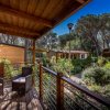 Veranda in legno con sedie, circondata da vegetazione e bungalow in legno.