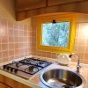Cucina con piano cottura a gas, lavandino circolare, piastrelle rosa e piccola finestra gialla.