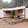 Una casa mobile bianca con veranda in legno, situata tra alberi alti.
