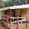 Casa mobile bianca con veranda in legno, tavolo e sdraio, circondata da alberi.