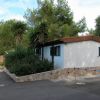 Casa bianca con tetto marrone e finestre verdi, circondata da piante e alberi.